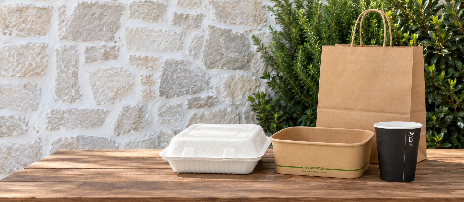Kraft takeaway containers, paper carry bag, fibre clamshell and takeaway cup on a wooden table